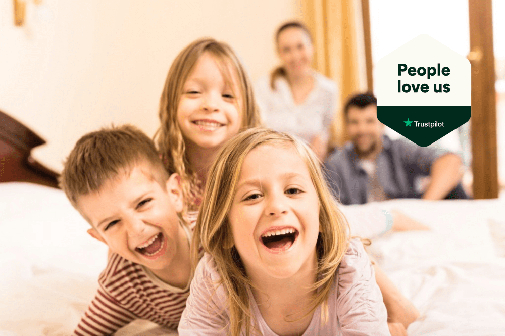 Three happy children playing on a hotel bed with parents behind