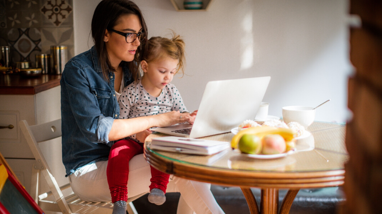 Parent holding a toddler and working on a laptop